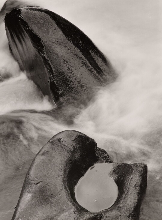 A black-and-white photograph of steam rising from two rocks, one with a pool of water in it.