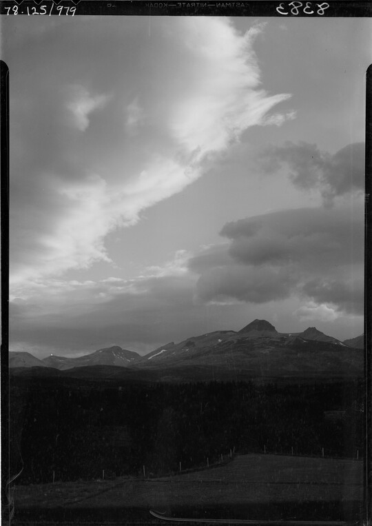 A black-and-white image of a dark mountain landscape under a cloudy sky.