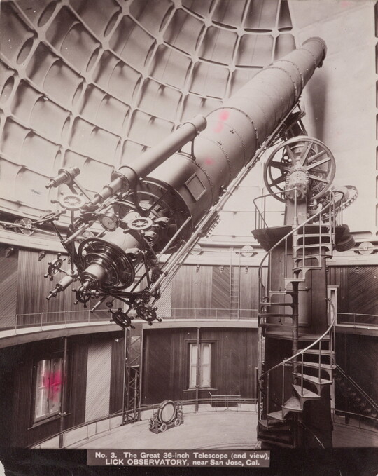 A sepia-toned photograph of a large telescope with complex gears on the end sitting atop a spiral staircase inside a domed structure.