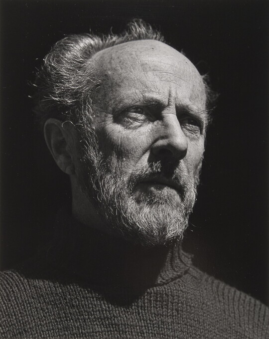 A black-and-white portrait photograph of an older, bearded White man wearing a turtleneck looking out into the distance.