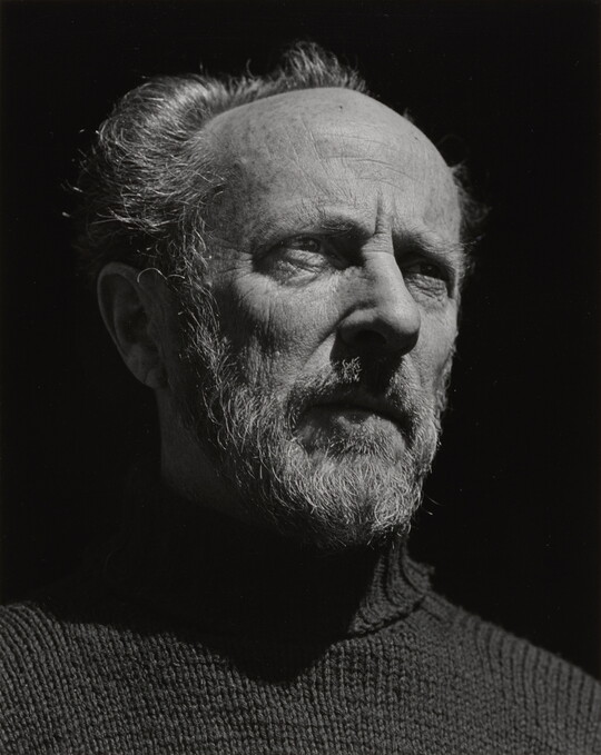 A black-and-white portrait photograph of an older, bearded White man wearing a turtleneck looking out into the distance.