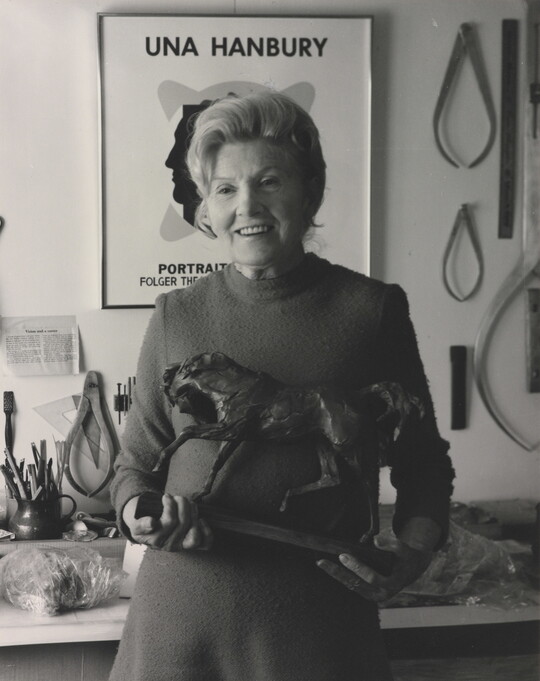 A black-and-white portrait of an older, White woman holding a horse sculpture in a studio.