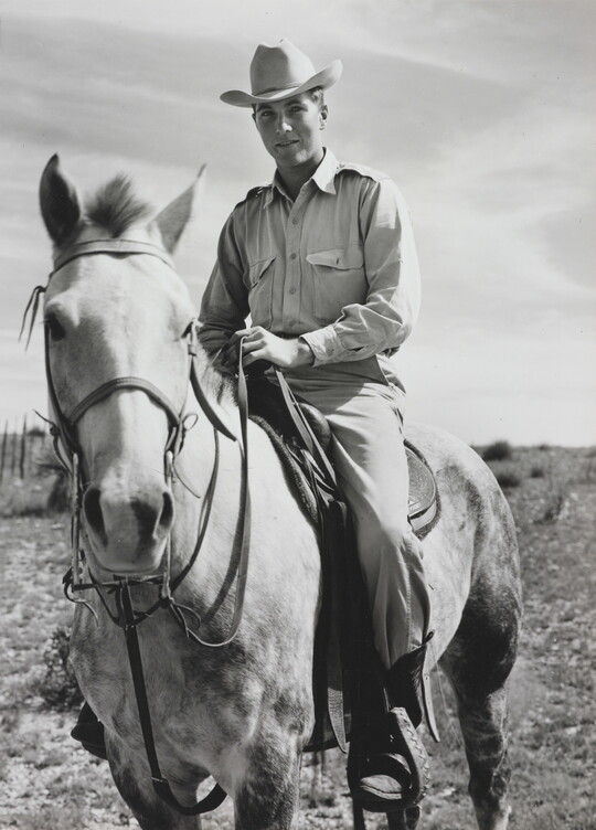 A black-and-white photograph of a White man in a cowboy hat sitting astride a dappled horse.