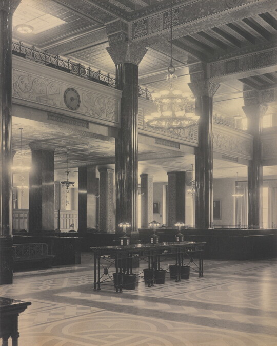 A black-and-white photograph of the interior of an ornate office lobby with inlaid floors, columns, and chandeliers.