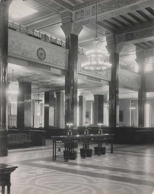 A black-and-white photograph of the interior of an ornate office lobby with inlaid floors, columns, and chandeliers.