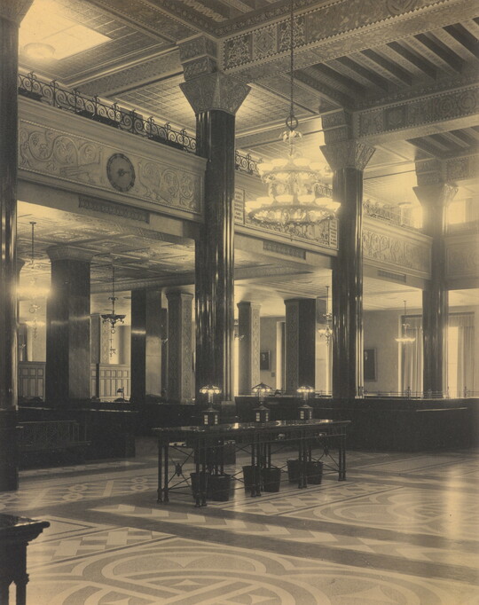 A black-and-white photograph of the interior of an ornate office lobby with inlaid floors, columns, and chandeliers.