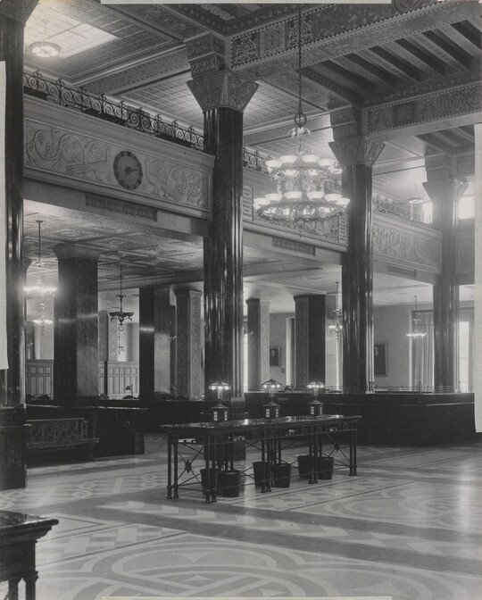 A black-and-white photograph of the interior of an ornate office lobby with inlaid floors, columns, and chandeliers.