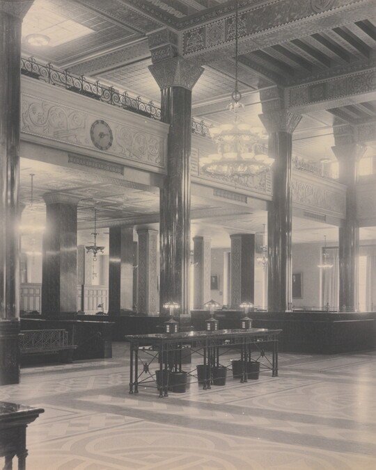 A black-and-white photograph of the interior of an ornate office lobby with inlaid floors, columns, and chandeliers.