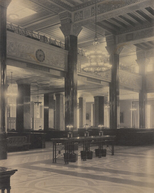 A black-and-white photograph of the interior of an ornate office lobby with inlaid floors, columns, and chandeliers.