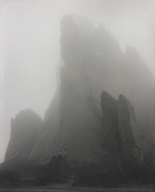 A black-and-white photograph of a large rock formation partially hidden by fog.