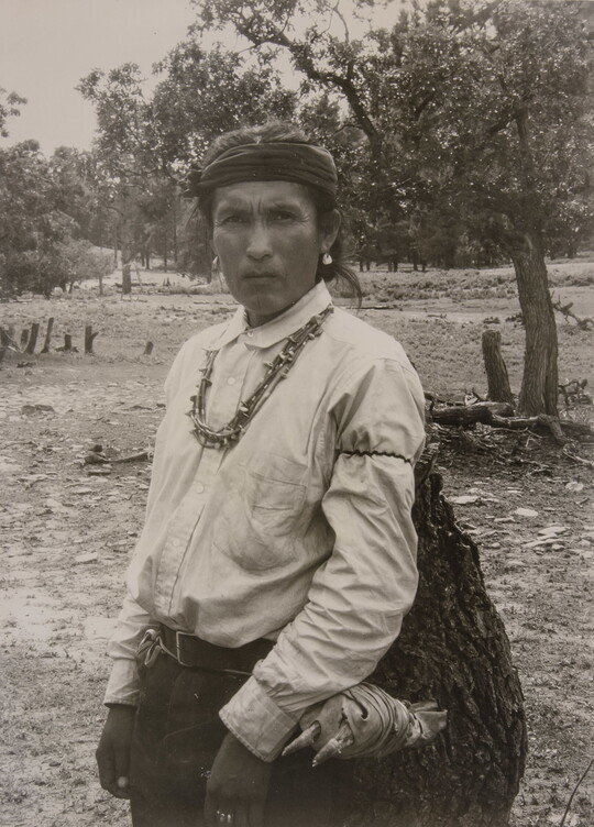 A sepia-toned photograph of an Indigenous man carrying a large bag.