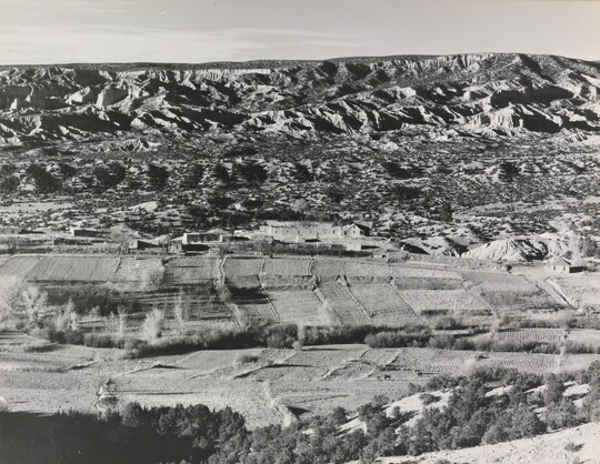 A black-and-white photograph of an aerial view of farms that run up against mountains.