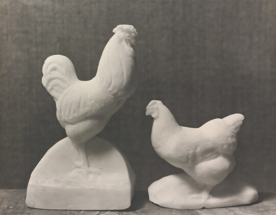 A black-and-white photograph of sculptures of a rooster and hen carved out of white soap.