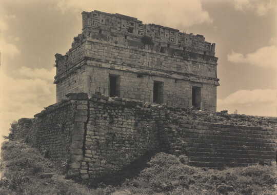 A sepia-toned photograph of a ruined stone temple in at the top of a crumbling stone staircase.