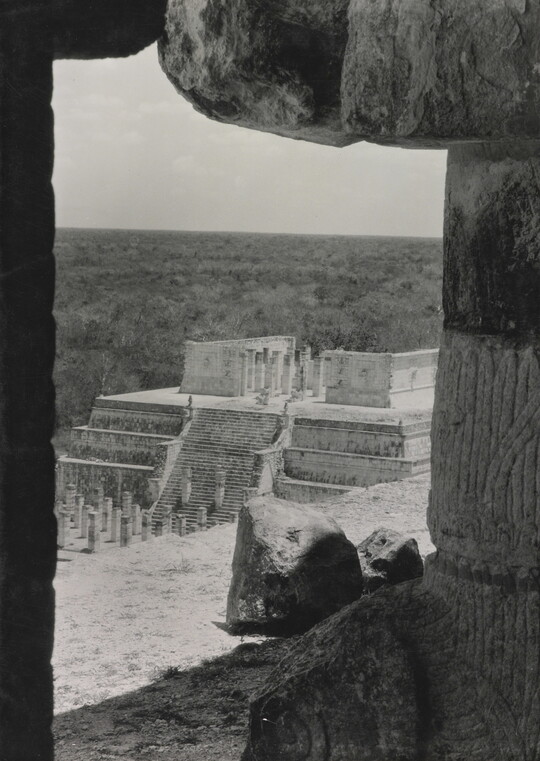 A black-and-white photograph of an ancient step pyramid viewed through a stone window.