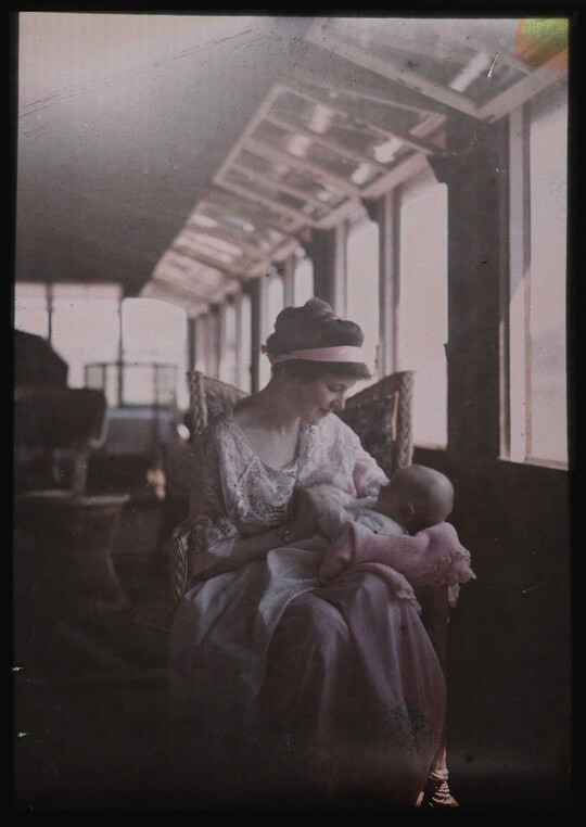 A color image of a seated White woman looking lovingly at an infant in her arms.