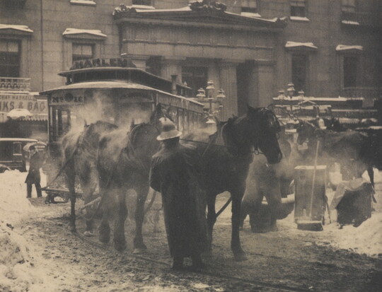 A black-and-white photograph of horses pulling a trolley on a busy street covered with slush and snow.