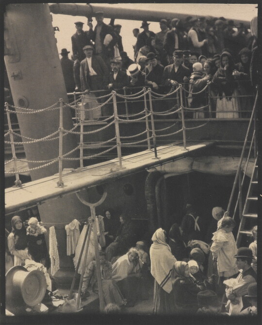 A black-and-white photograph of people outside on two decks of a crowded ship.