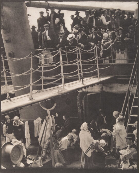 A black-and-white photograph of people outside on two decks of a crowded ship.