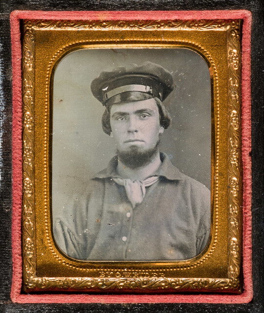 A black-and-white photograph in a gold frame and case of a young man posed in a military hat.