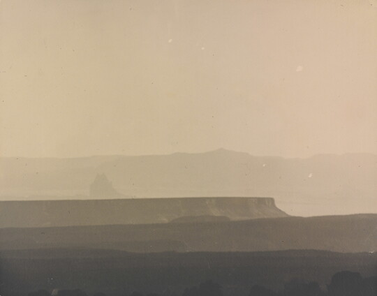 A sepia-toned photograph of a hazy mesa and distant mountains.