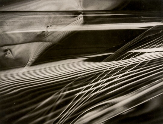 An abstract black-and-white photograph of layered sets of parallel rays of light that resemble guitar strings intersecting with one another.