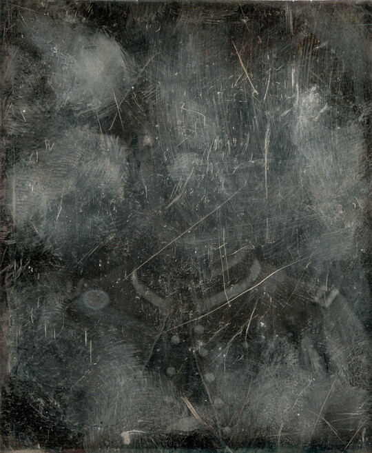 A black-and-white photograph of a man in military dress, mostly obscured by marks and scrapes on the surface.