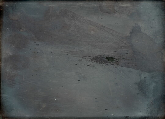 An obscured black-and-white photograph of gray, monochromatic forms, including an angular shape across the top right corner and a splatter in the center.