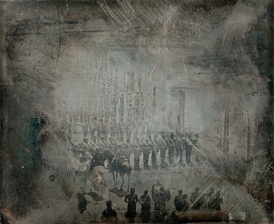 A dark, heavily scratched black-and-white photograph of rows of soldiers facing two figures on horseback and another group of soldiers.