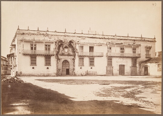 A sepia-toned photograph of an intimidating two-story structure, awash in light, with an ornate entrance and spikes across the top.