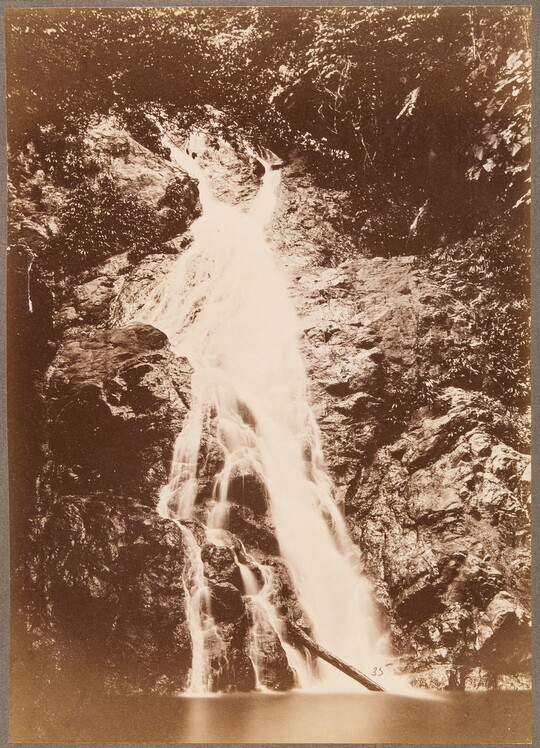 A sepia-toned photograph of a waterfall going down a rocky hill toward a river.