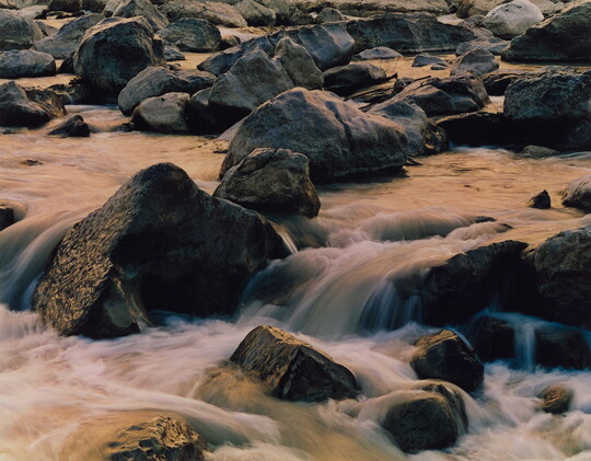 An up-close color photograph of water rushing over rocks in a river.