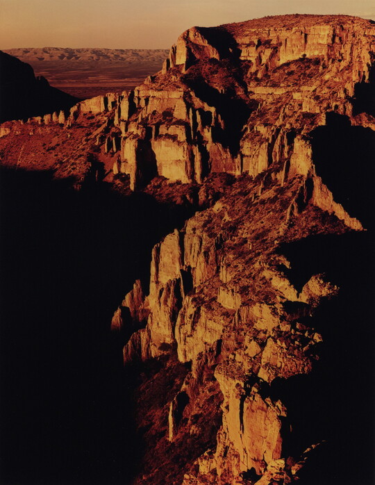 A color photograph of a rocky canyon landscape, the light reflecting off some of the cliff faces.