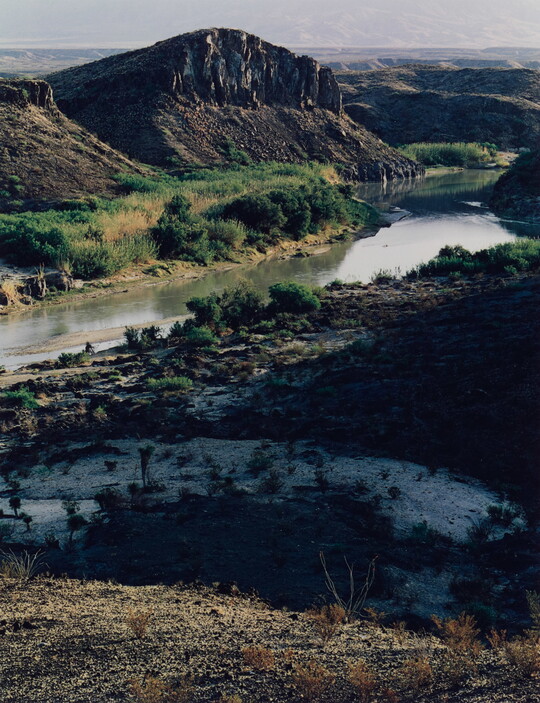 A color photograph of a winding river surrounded by rocky cliffs and vegetation.