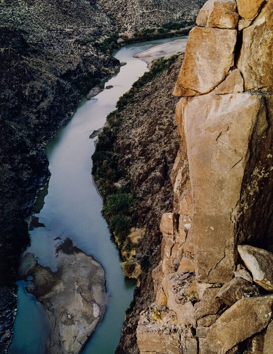 A color photograph taken from above of a river running through a canyon below steep rocky cliffs.