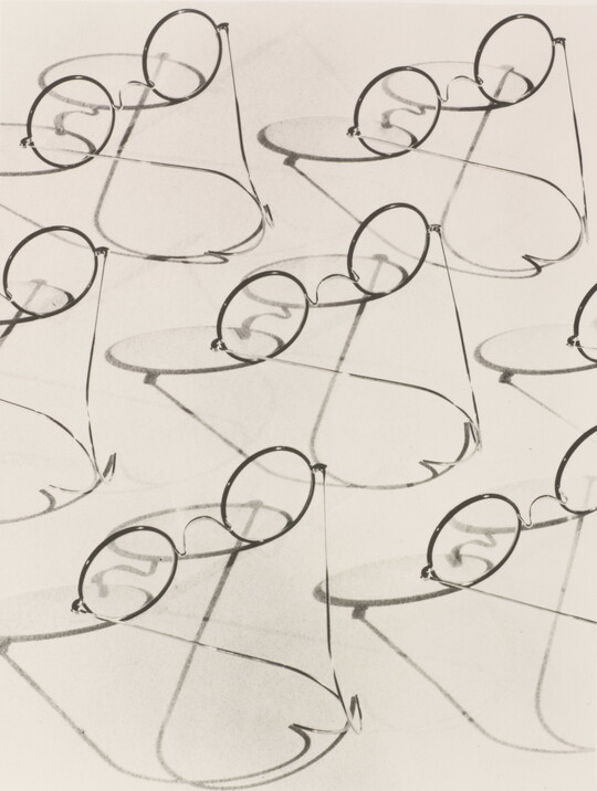 A black-and-white photograph of multiple granny-style eyeglasses and their shadows.