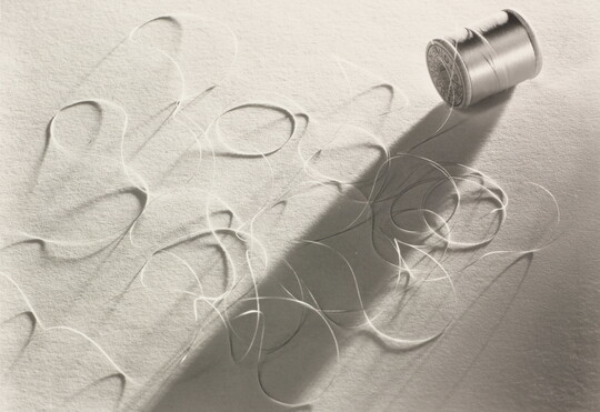 A black-and-white photograph of a spool of thread laying on its side with loose thread in loops around it.