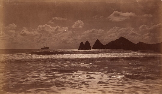 A sepia-toned photograph of a boat heading toward a rocky coast on an ocean.