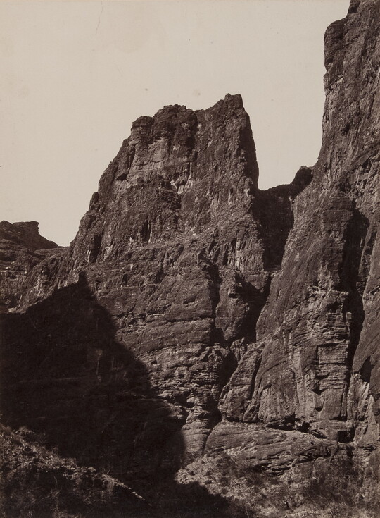 A black-and-white photograph of tall, sheer cliffs; the shadow of a cliff on the opposite side partially covers the base of one cliff.