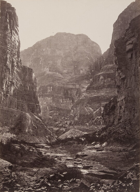 A black-and-white photograph of the bottom of a rocky canyon surrounded by tall cliffs.