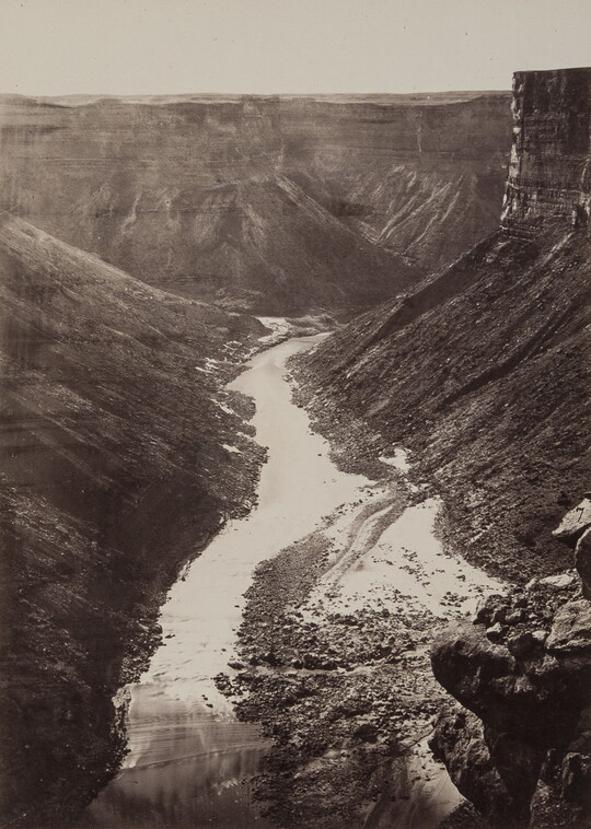 A black-and-white photograph, taken from a high elevation, of a river surrounded by cliffs and steep hillsides.