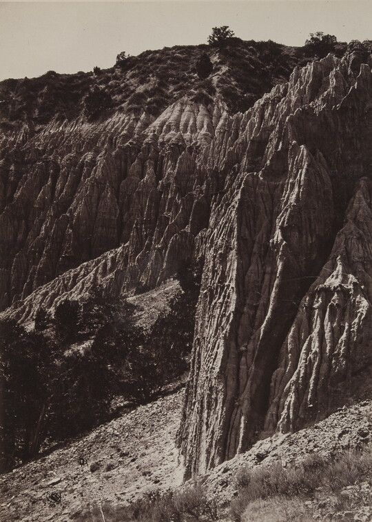 A black-and-white photograph of rocky cliffs jutting up from a desert landscape.