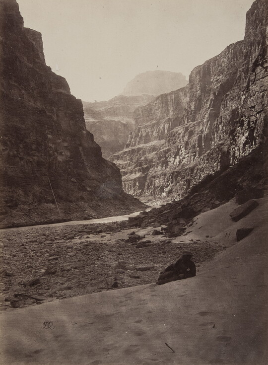 A black-and-white photograph of a river running through a canyon surrounded by tall cliffs.