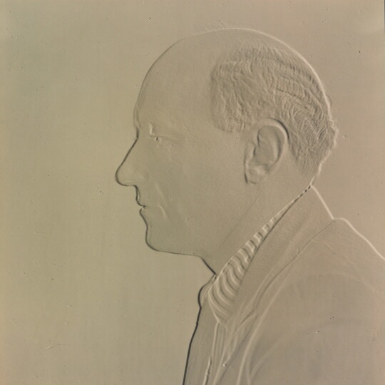 A white embossed photograph of a balding White man in profile.