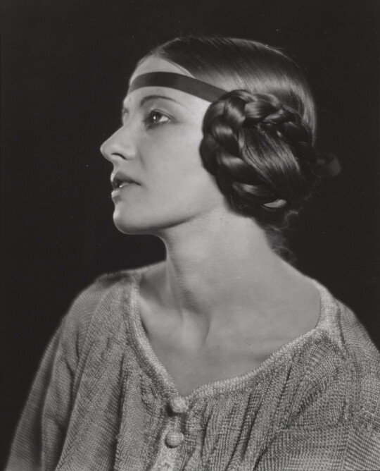 A black-and-white portrait of a White woman in profile with braided hair covering her ear.