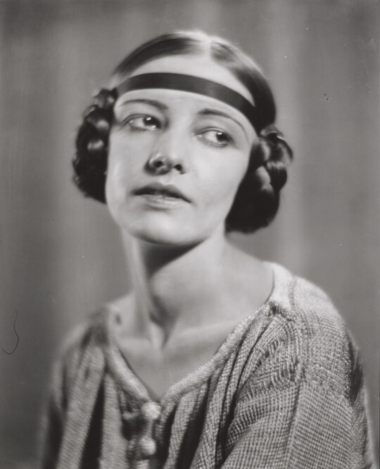 A black-and-white portrait of a White woman with her hair braided into buns on the sides of her head.
