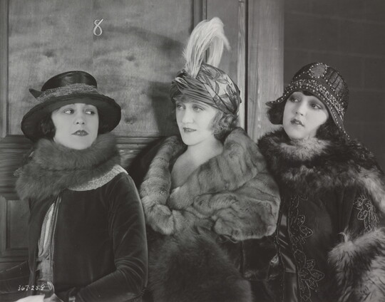 A black-and-white photograph of three elaborately-dressed White women, all wearing hats and fur stoles.