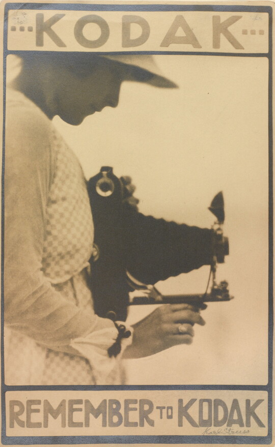 A sepia-toned advertisement poster for Kodak of a White woman in profile holding a large camera and looking down into the viewfinder.