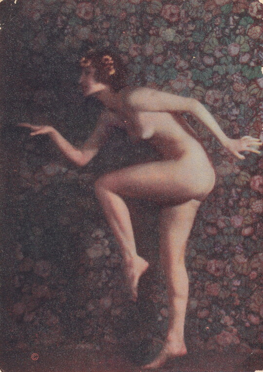 A faded color photograph of a nude, fair-skinned women posed as if in the middle of a dance, with one leg bent, arms out, and yellow flowers in her hair.