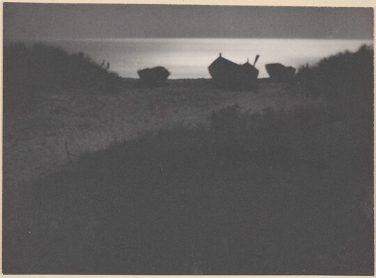 A black-and-white photograph of three rowboats in silhouette against a moonlit sea with a beach and grasses in the foreground.